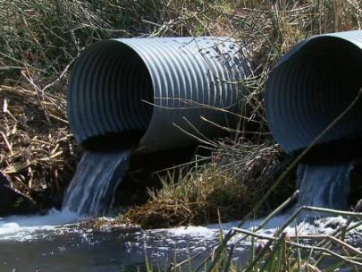 Image of water draining from pipes in a field.