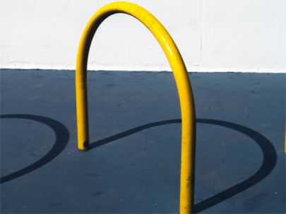 A curved, yellow bike rack casting a shadow on the concrete ground.
