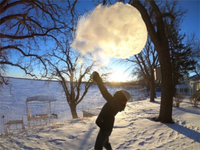 A person throwing boiling water into freezing air. The boiling water appears to have turned into a cloud.