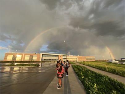 A rainbow in front of dark clouds over a school building. 