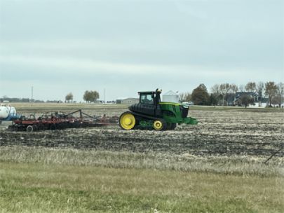 A green tractor cultivating the soil in a field. 