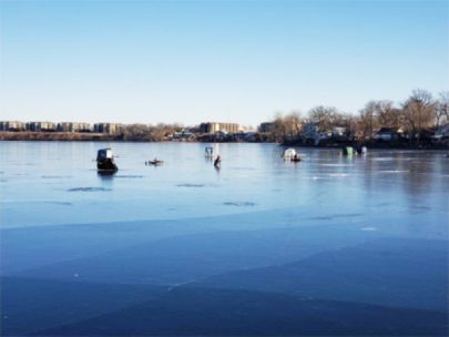 A frozen lake with five ice fishing tents on it. 